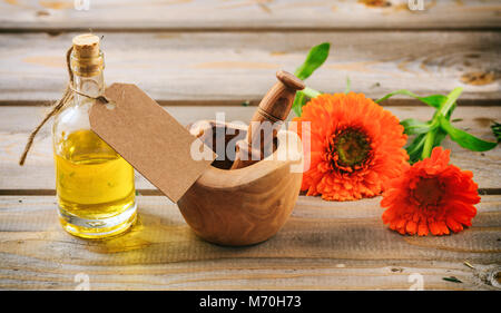 Calendula o fiorrancio olio essenziale e fresco ramoscello di fioritura in un mortaio di legno, tavolo in legno, tag vuoto, spazio per il testo Foto Stock