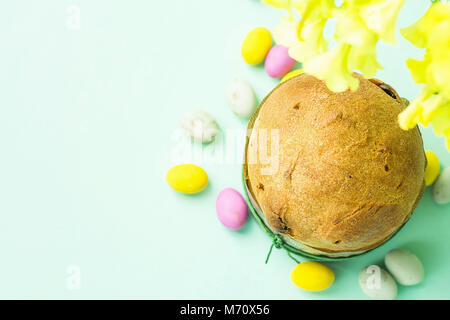 Home Pasqua al forno Torta dolce panettone a forma di carta multicolore cioccolato granuloso Candy uova sparsi sul piano portapaziente turchese primavera fiori gialli Foto Stock