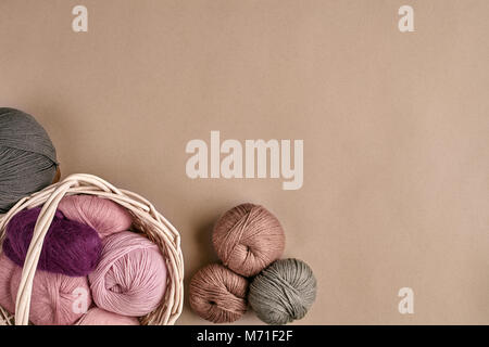 Palline di filato e aghi da maglia. Filato colorato per lavorazione a maglia in un recipiente di vimini su un sfondo beige. Foto Stock