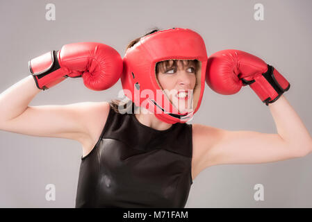 Donna boxer con un espressione facciale indossando un headguard rosso e rosso guantoni da pugilato, circa 2018 Foto Stock