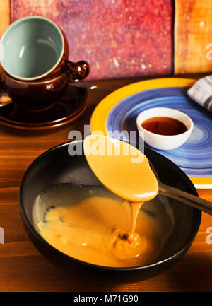 Esecuzione di caramello cade cucchiaio in ceramica nera sulla vaschetta di colore marrone scuro tabella Foto Stock