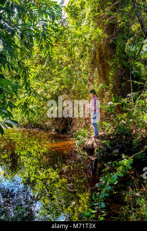 Il Banteay Srei, Cambogia - 11/12/2016: un adolescente Khmer cambogiano ragazza pesci con un fatti in casa a base di canna da pesca in un piccolo flusso di giungla vicino al suo telecomando vill Foto Stock