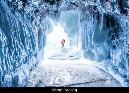 Paesaggio invernale, congelati caverna di ghiaccio con il giovane fotografo in piedi da solo. Viaggiare in inverno Foto Stock