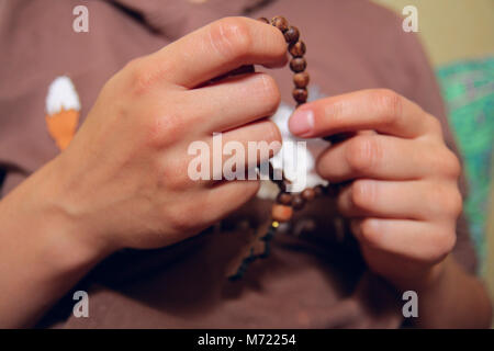 Perline di legno in mano. Donna orante indossando i grani del rosario. Close up mani femminili. Foto Stock