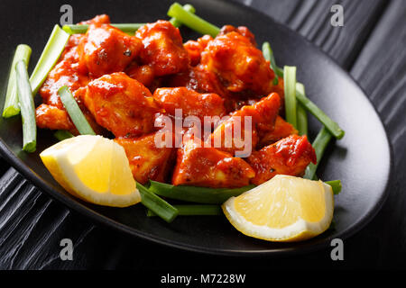 Tradizionale piatto indiano 65 di pollo con le cipolle verdi e limone close-up su una piastra su un piano orizzontale. Foto Stock