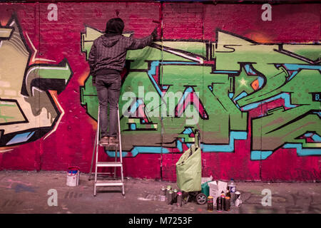 Uomo in piedi su una scala dipinto graffiti, a Leake Street tunnel, Londra, vicino alla stazione di Waterloo. Foto Stock