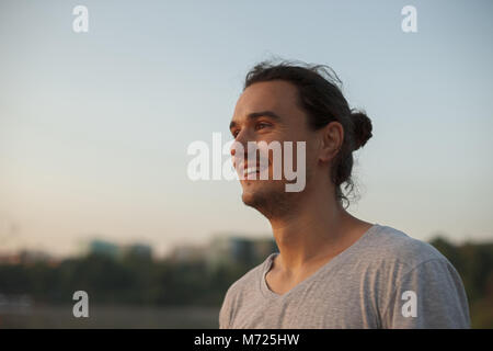 Profilo di uomo bello sorridere mostrando i denti nel parco sul lago mentre cercano di sunrise. Ritratto di atletica capoeira positivo uomo sulla città essere Foto Stock