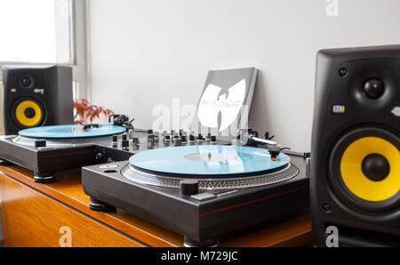 Un DJ set-up con due giradischi, mixer e monitor altoparlante. Wu-Tang libro manuale appoggiata sulla parete. Tutti impostati su legno tavolo ripiegato. Impianto di rosso in backg Foto Stock