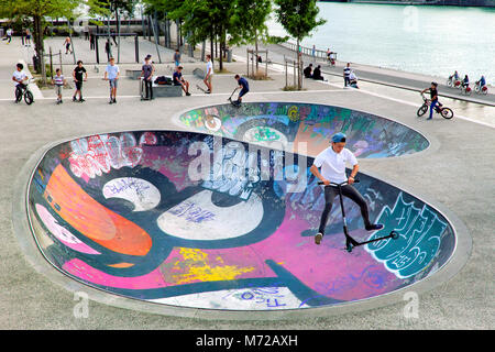 Ragazzo facendo mid-aria scooter trucco in colorate skate park bowl, Lione, Auvergne-Rhône-Alpes Regione, Francia Foto Stock