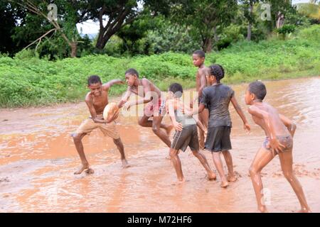 I bambini giocare a rugby in un mudbath al di fuori di un villaggio di campagna di Figi. Heavy Rain aveva invaso il loro campo da gioco ma questo non ha fermato il loro amore per il rugby. La loro gioia e la loro esuberanza è normale vedere in una comunità che è estremamente povero. Foto Stock