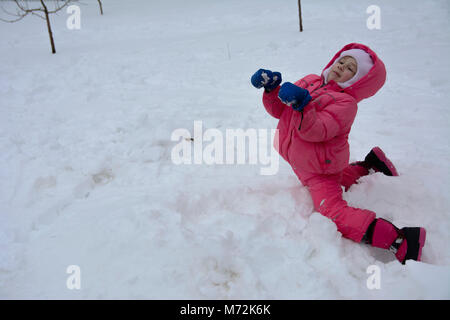 Una bambina in una complessiva rosso fa un pupazzo di neve. Il gioco del bambino in inverno. Marzo 2018 in Ucraina. Foto Stock