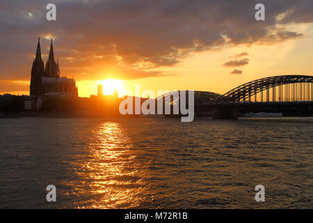 Tramonto tra la cattedrale di Colonia (Kölner Dom) e Hohenzollern ponte che attraversa il fiume Reno. Foto Stock