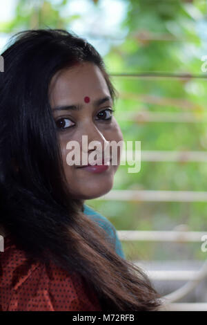 Una bella signora bengali, in piedi di fronte a una finestra è girare la testa per guardare qualcuno. Foto Stock