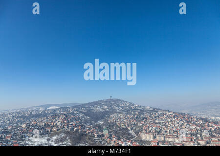 Vista aerea delle colline della periferia di Sarajevo, Bosnia ed Erzegovina durante un inverno freddo pomeriggio di neve che ricoprono tutto. La torre della TV di t Foto Stock