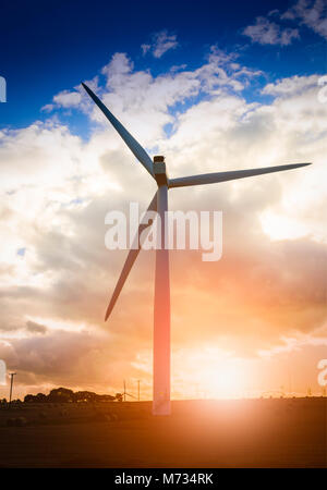 Turbina eolica con le balle di paglia su terreno coltivato al tramonto Foto Stock