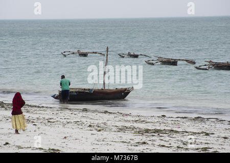 Sambuco tradizionale di barche da pesca a bassa marea nella spiaggia di Jambiani Zanzibar Tanzania con alghe marine agricoltore donna e la sabbia bianca Foto Stock