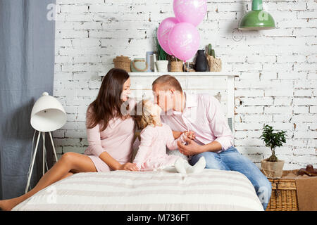 Famiglia giovane seduto sul letto. Baby girl bacia il padre Foto Stock