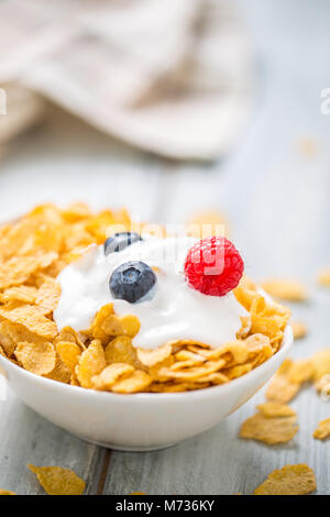 Cornflakes. Piatto di cornflakes con yogurt, mirtilli e lamponi sul tavolo da cucina. Foto Stock