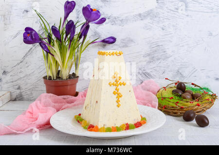 Cagliata tradizionale torta di Pasqua con frutta candita e uova di cioccolato, fiori di primavera crocus sulla vacanza sfondo luminoso. Pasqua cottage cheese dess Foto Stock