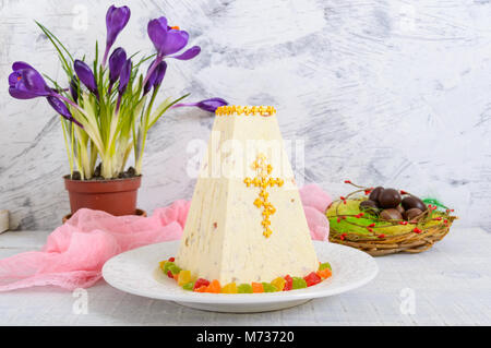 Cagliata tradizionale torta di Pasqua con frutta candita e uova di cioccolato, fiori di primavera crocus sulla vacanza sfondo luminoso. Pasqua cottage cheese dess Foto Stock