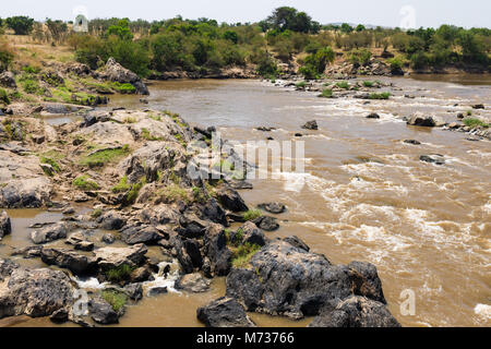 Il fiume di Mara che fluisce nel Maasai Mara riserva nazionale, le rocce e la vegetazione in linea le sponde in una giornata di sole, Kenya Foto Stock