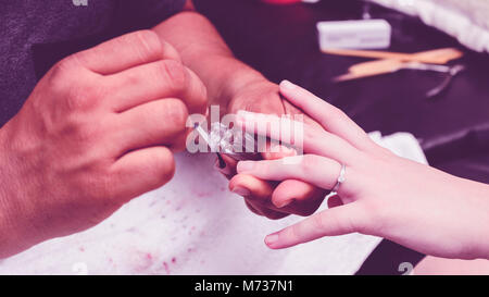 Manicurist applicando una base trasparente sulla donna le mani prima di smalto per unghie pittura procedura. Foto Stock