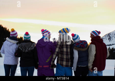 Sei persone guardando il tramonto dal fuoco mentre è in vacanza sciistica momenti di vacanza del team nelle alpi svizzere Foto Stock