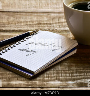 Primo piano di un notebook con il testo poesia giorno scritto in esso, una penna e una tazza di caffè su una tavola in legno rustico Foto Stock
