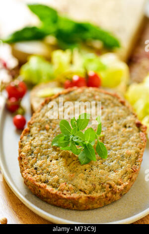 Primo piano di alcuni veggie hamburger di melanzane e altre verdure in una piastra, posto su una tavola in legno rustico Foto Stock