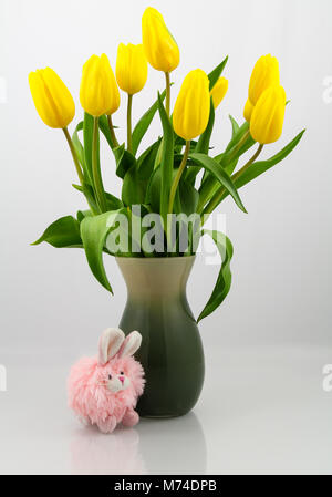 Bouquet di tulipani gialli nel vaso verde con un piccolo giocattolo coniglietto rosa il convogliamento di una molla o di un tema di pasqua. Foto Stock