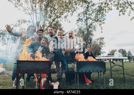 Gli amici sul barbecue uno in gasmask aprire il fuoco la cottura di carni bovine Foto Stock