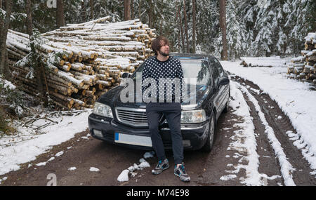 Uomo in piedi vicino al nero car ho la neve invernale forest Foto Stock
