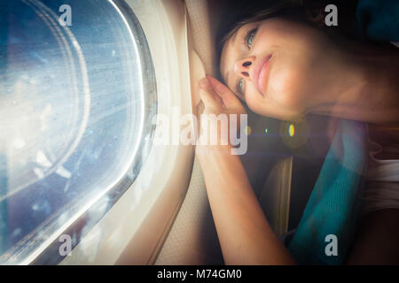 Felice, femmina passeggero aereo godendo la vista dalla finestra cabon oltre il cielo blu (SHALLOW DOF; flare intenzionale) Foto Stock