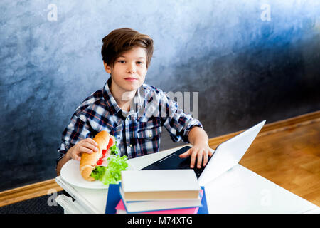 Ritratto di ragazzo adolescente mangia un panino e la navigazione sul web Foto Stock