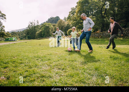 Tre generazioni la famiglia sono giocare a calcio insieme in un campo. Ci sono due ragazzi, il loro padre e il nonno. Foto Stock