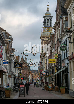 KAMPEN, Paesi Bassi - 30 novembre 2017: Oudestraat via commerciale con la stagione invernale luci su un pomeriggio freddo. Sullo sfondo la Nieuwe Toren Foto Stock