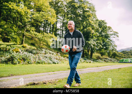 Senior l uomo è il gioco del calcio presso il campeggio con i suoi nipoti che non può essere visto. Foto Stock