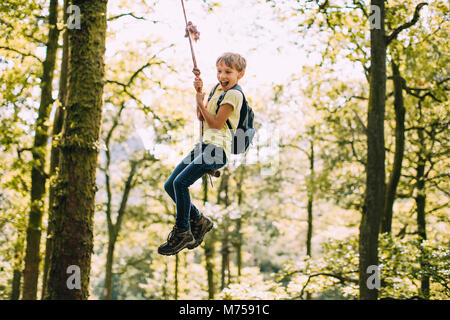 Little Boy sta avendo un andare su una corda swing ha trovato durante le escursioni. Foto Stock