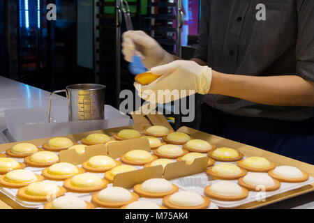 Le donne chef pasticcere stanno prendendo una spazzola di pasticceria e spazzolatura dell'uovo sbattuto sulla parte superiore della torta di formaggio in cucina al panificio. Foto Stock