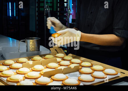 Le donne chef pasticcere stanno prendendo una spazzola di pasticceria e spazzolatura dell'uovo sbattuto sulla parte superiore della torta di formaggio in cucina al panificio. vintage foto e film styl Foto Stock