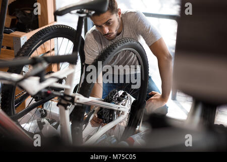 Uomo di ispezionare una ruota di bicicletta per allineamento. Lavoro meccanico di fissaggio per una bicicletta in officina. Foto Stock
