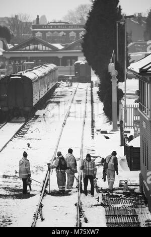 Scena in bianco e nero, stazione ferroviaria di Severn Valley Kidderminster sulla neve. I lavoratori ferroviari si sono impegnati a fondo per garantire che il vapore sia all'avanguardia! Lavoro di squadra nel Regno Unito. Foto Stock