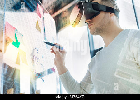 Attento uomo in realtà virtuale bicchieri cercando grave mentre si tiene un marcatore Foto Stock