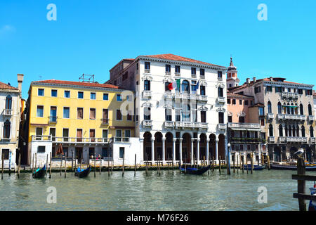 Gondole ormeggiate lungo il Canal Grande a Venezia con il rosso e bianco striato posti di ormeggio su una giornata d'estate con un brillante blu cielo privo di nuvole Foto Stock