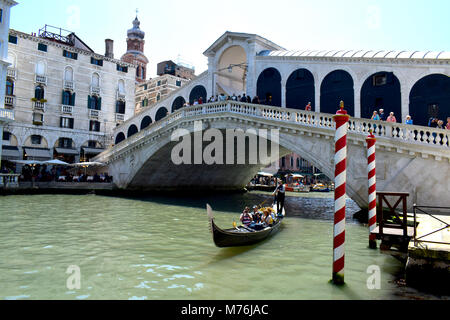 Una gondola passando sotto il ponte di Rialto, Sestiere San Polo, Venezia, città metropolitana di Venezia, Italia, con il rosso e bianco striato posti di ormeggio. Foto Stock