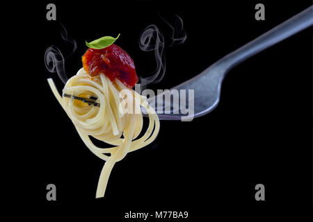 La cottura a vapore gli spaghetti con sugo di pomodoro e basilico sulla forcella, isolati su sfondo nero. Close-up shoot, Foto Stock