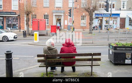 Meteo, Bridport, Inghilterra, Regno Unito venerdì 9 marzo 2018. Due donne siedono su una panchina in chat in Bridport High Street come si inizia a drizzle. Il grigio e piovoso le condizioni vengono impostate per continuare per tutto il weekend con il miglioramento e il lunedì, ma le temperature saranno più caldi del ritardo. Credito: PQ Immagini/Alamy Live News Foto Stock