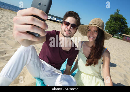 Splendida coppia giovane seduto alla spiaggia e facendo selfie Foto Stock