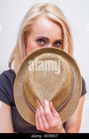 Ritratto di giovane donna bionda che copre il volto con estate hat. Isolato su sfondo bianco. Foto Stock