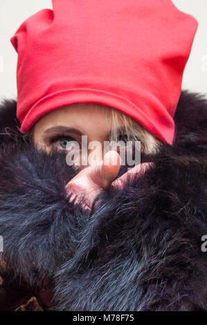 Red Hat donna bionda con si copre la faccia con il nero soffice pelliccia e puntando sulla fotocamera con il dito indice. Foto Stock
